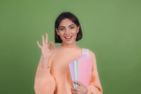 Smiliing young girl student doing an okay sign holding her books in her arm