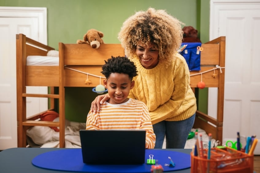 A mother standing next to her child during their online tutoring lesson on GoStudent