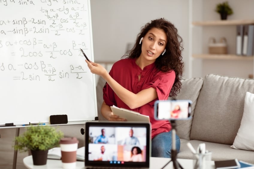 An online maths tutor teaches in front of her camera using a whiteboard