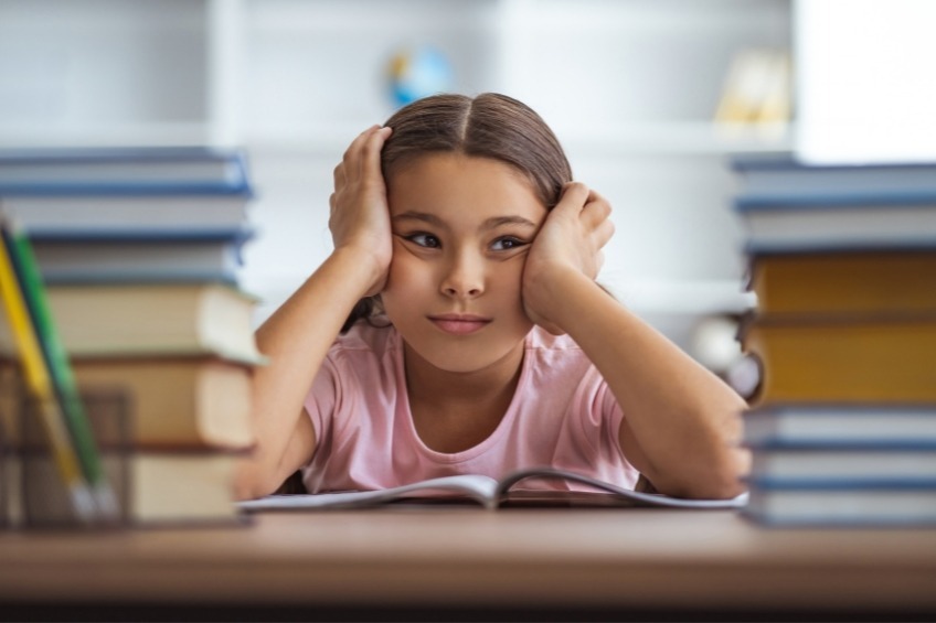 Fillette dyslexique demotivee assise sur son bureau devant son livre visage entre ses mains