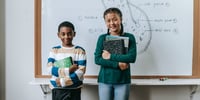 niño y niña estudiantes hacen una presentación oral frente a la pizarra