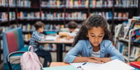 girl reading a book at a table in the library
