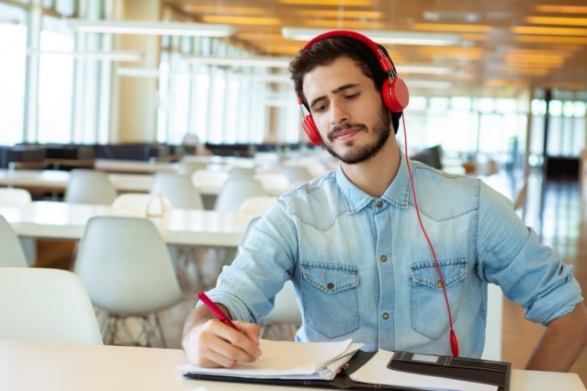 Jeune adulte prenant des notes et ecoutant un podcast BBC pour preparer le toeic