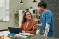 Professeure particulier assise au bureau souriant et ecoutant son eleve