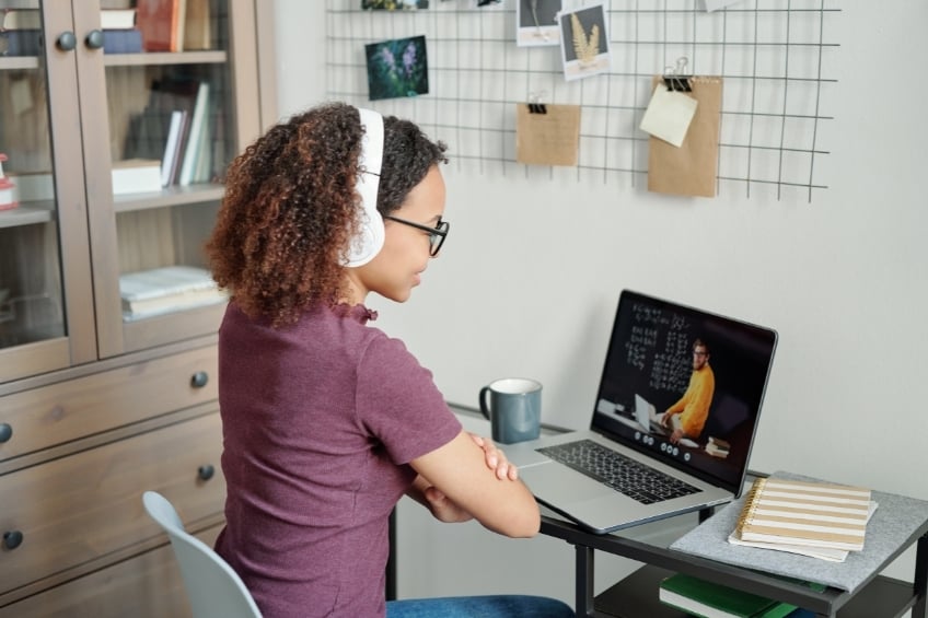 Student wearing headphones learning English via video tutoring on a laptop.