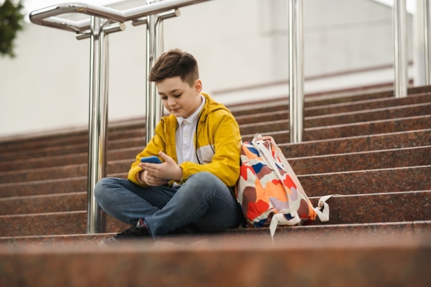 Teenage boy sitting outside on steps by his school using an AI for emotional support