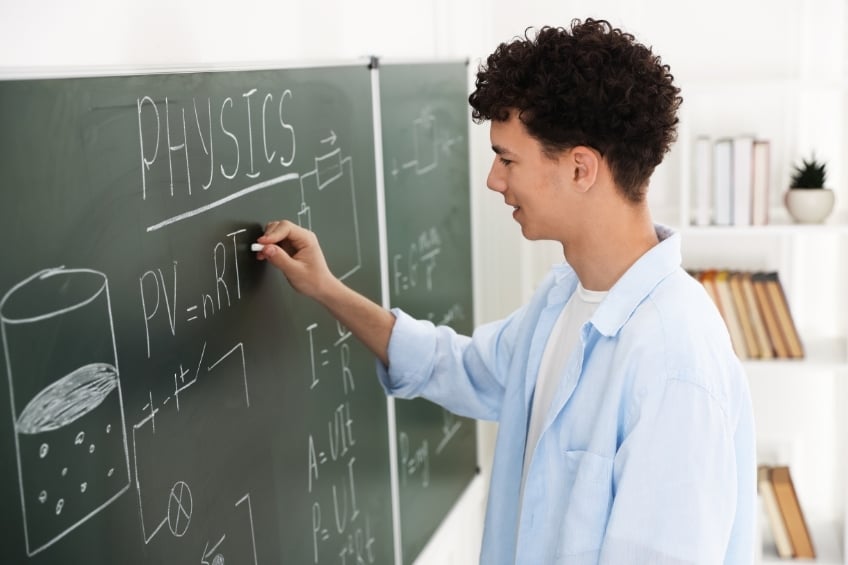 Un lyceen ecrit des formules sur un tableau en cours de physique chimie