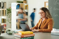 Une maitresse assise sur son bureau utilisant son ordinateur
