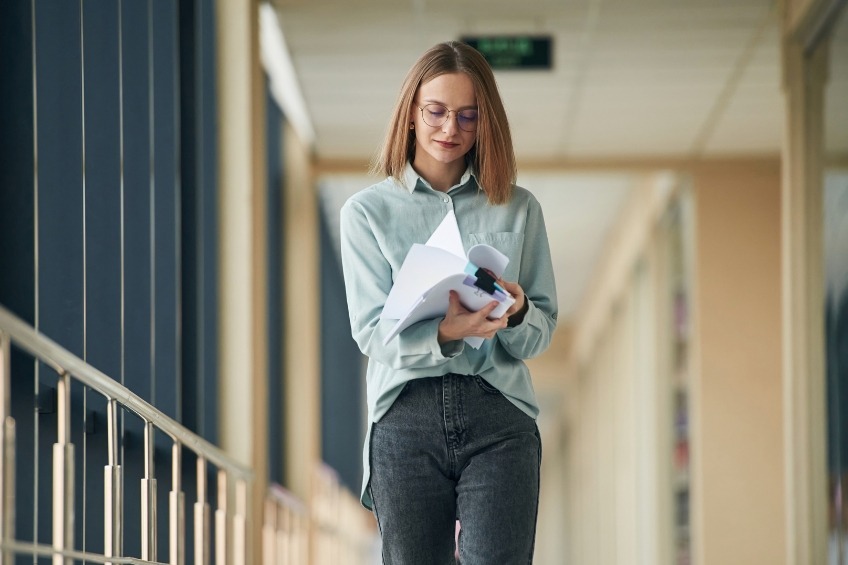 student-reading-gcses-exam-papers-walking-school-corridor-glasses-mint-shirt