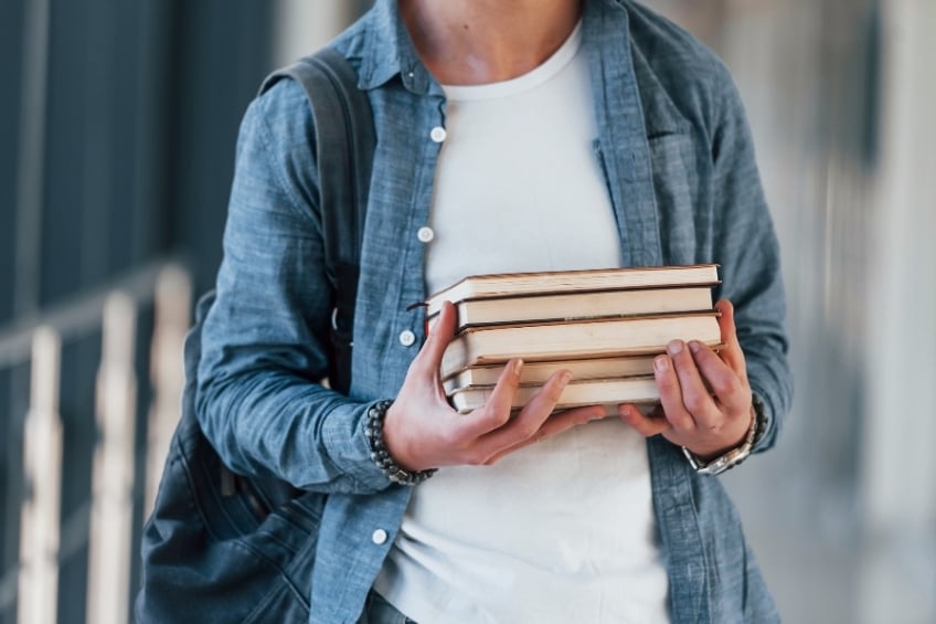 un adulte tient un pile de livres pour etudier et apprendre langlais seul