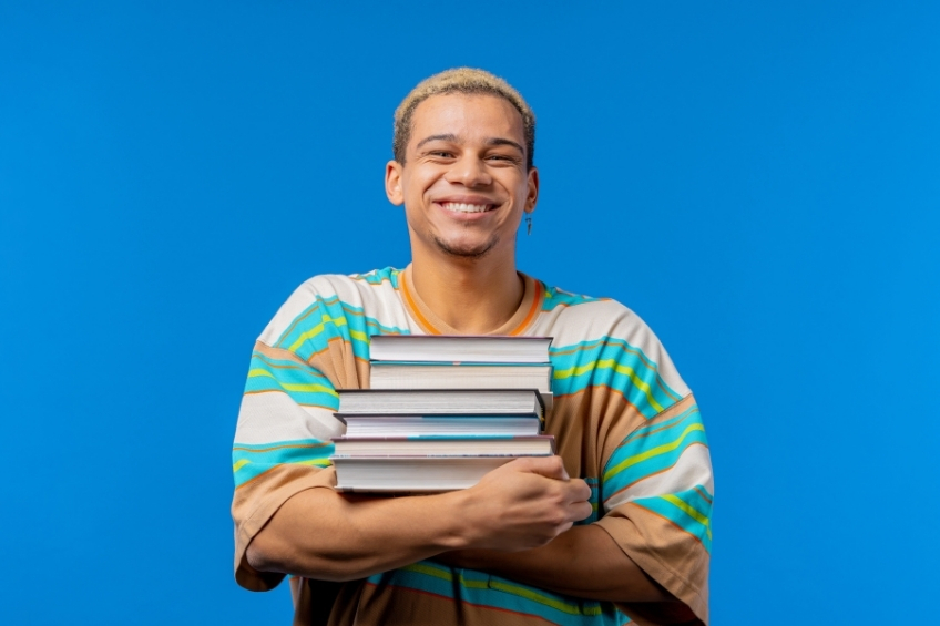 Jeune adulte tenant une pile de livres dans ses bras pour preparer le TOEIC