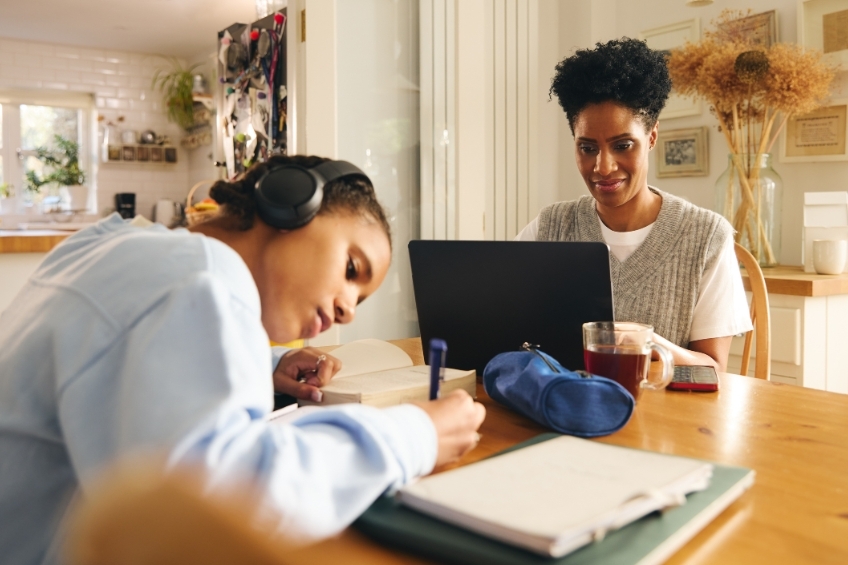 Teenage girl studying and reviewing textbooks next to her mom before school starts