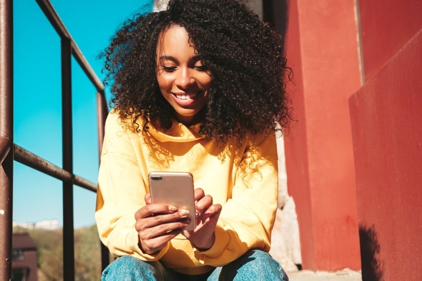 femme-souriante-teste-alternatives-a-duolingo-smartphone-exterieur